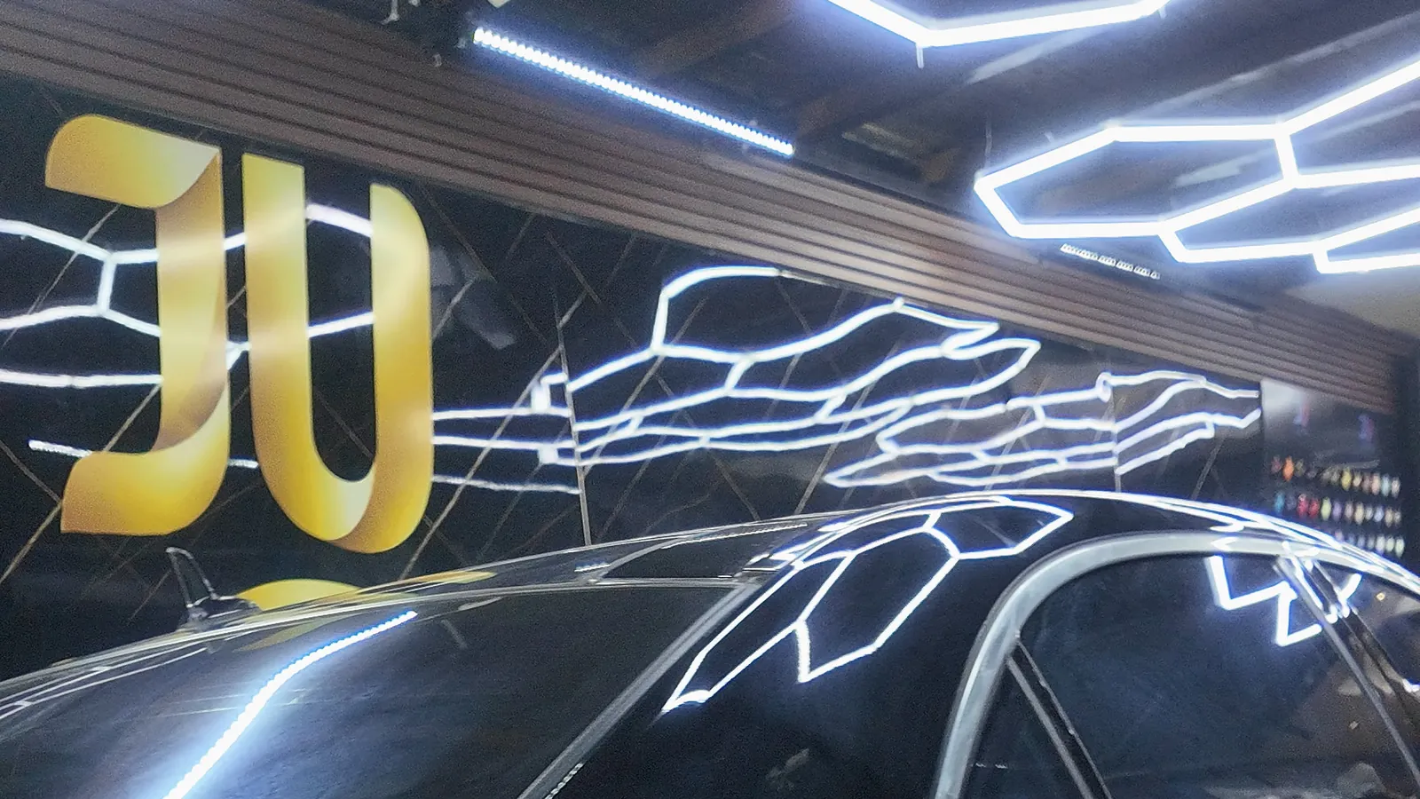 Side of a glossy black Mercedes S500 under the hexagon lights during full-body clear gloss PPF installation at JU Riyadh Center