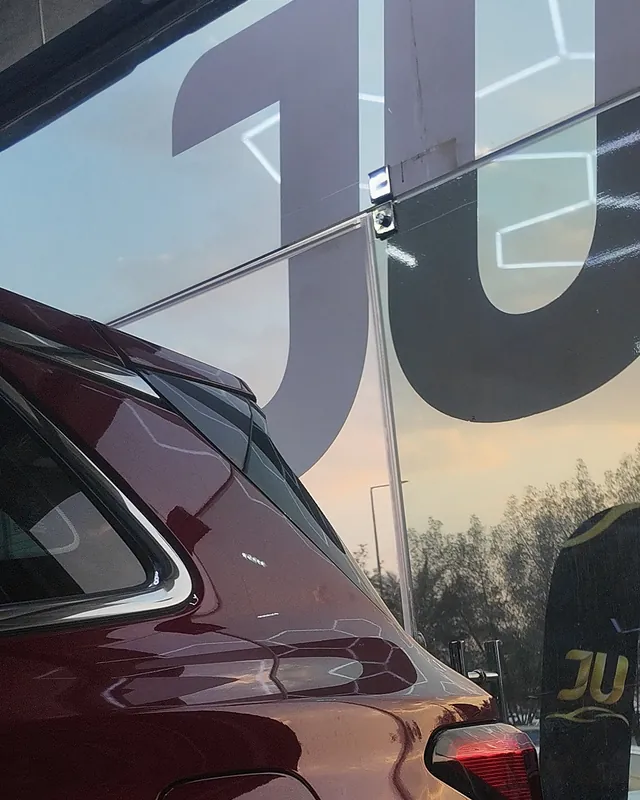 Red Ford Territory beside the large JU letters on the JU Riyadh Center glass during full-body clear gloss PPF installation